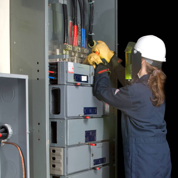 Female Electrician with protective clothing performing work in an energized panel